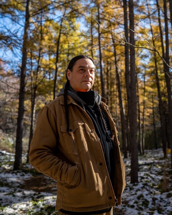 A man in a beige jacket stands in a yellow forest.