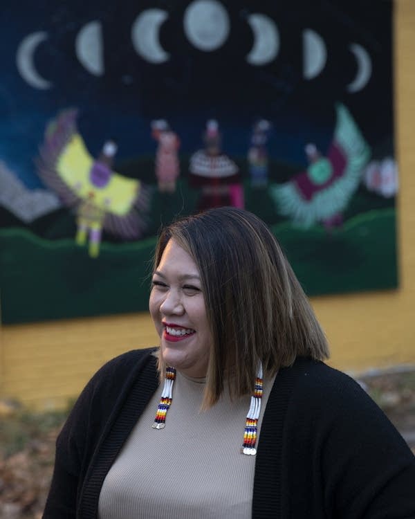 A woman smiles as she stands in front of a mural 
