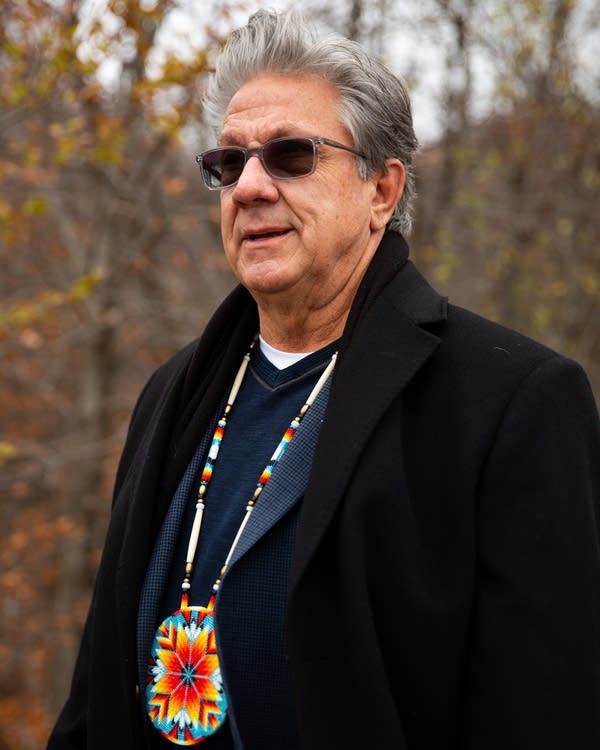 A man wearing a beaded necklace stands outside.