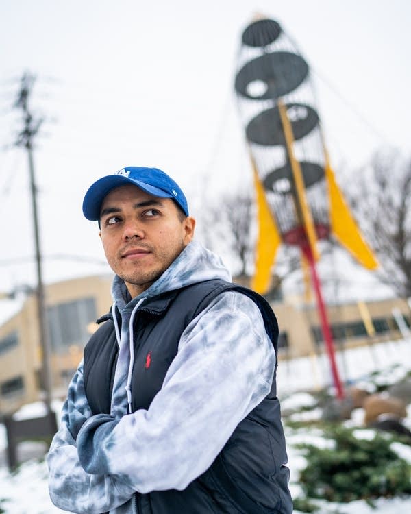 A man stands with arms crossed in front of a rocket ship sculpture.