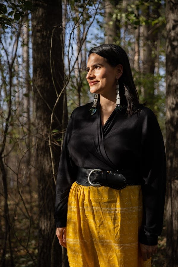 A woman in a black shirt and yellow skirt stands in a forest.
