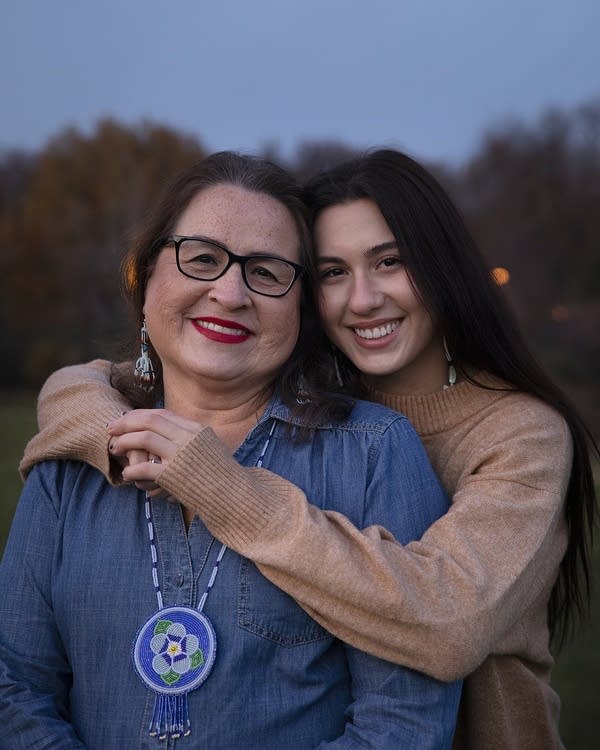 A young woman embraces her mother outside near dusk.