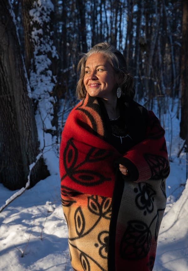 A woman wears a red blanket with floral designs around her shoulders. 